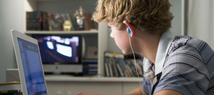 Young boy in bedroom using laptop and listening to